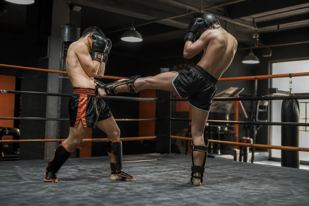 Deux boxeurs thaï en garde haute face à face sur un ring, l’un allongeant un coup de pied frontal pour maintenir l’autre à distance